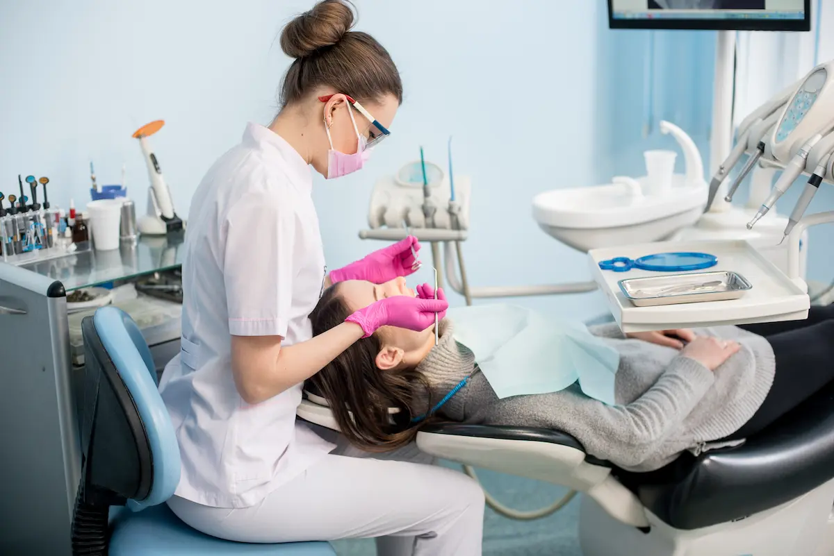 Dentist wearing pink gloves and mask examining a patient's mouth in a dental clinic.